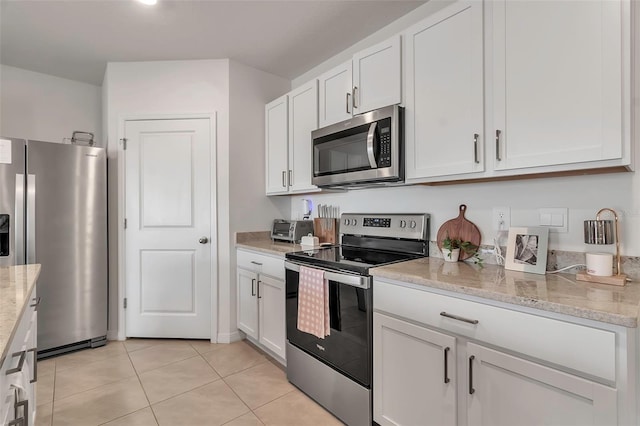 kitchen with a toaster, white cabinets, appliances with stainless steel finishes, light stone countertops, and light tile patterned flooring