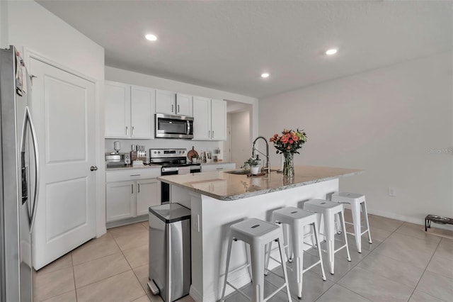 kitchen with light tile patterned floors, stainless steel appliances, a sink, a kitchen bar, and a center island with sink