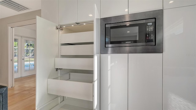 room details with white cabinetry, stainless steel microwave, light hardwood / wood-style floors, and french doors