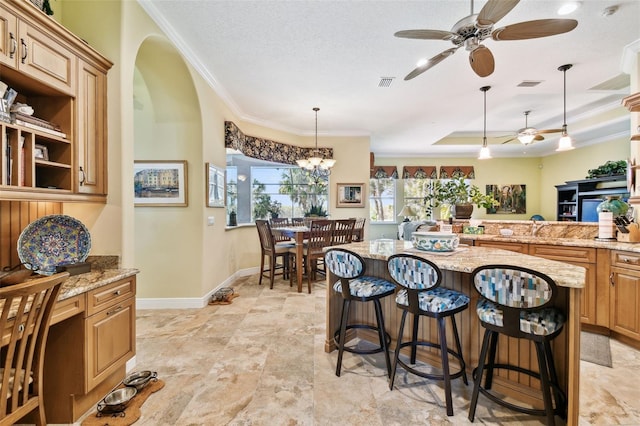 kitchen featuring a breakfast bar, decorative light fixtures, ornamental molding, a tray ceiling, and light stone countertops