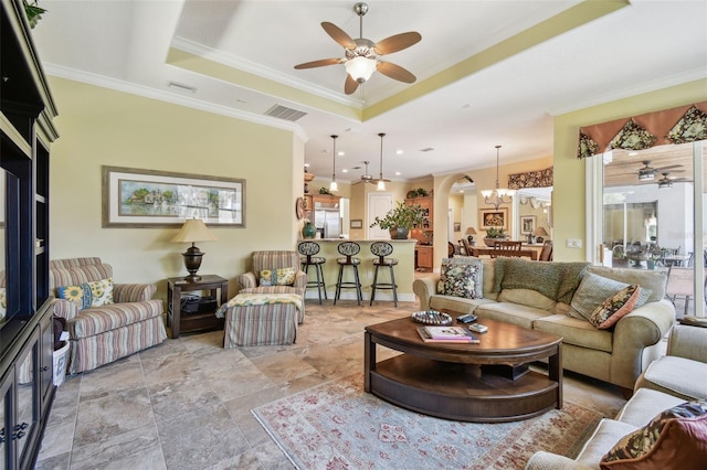 living room featuring ornamental molding, a raised ceiling, and ceiling fan with notable chandelier