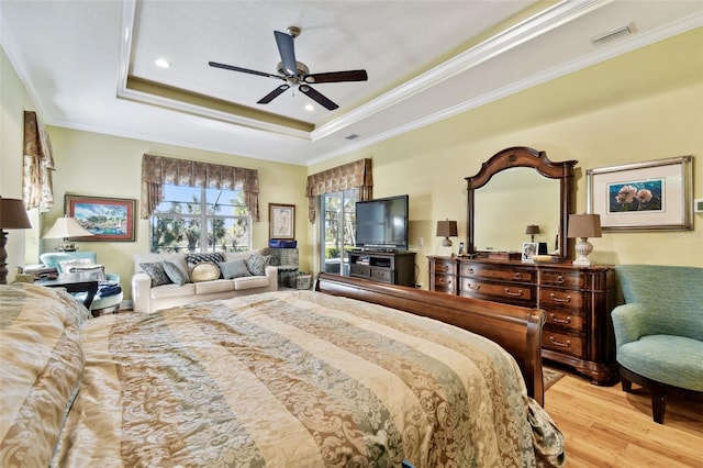 bedroom with a tray ceiling, ornamental molding, ceiling fan, and light wood-type flooring