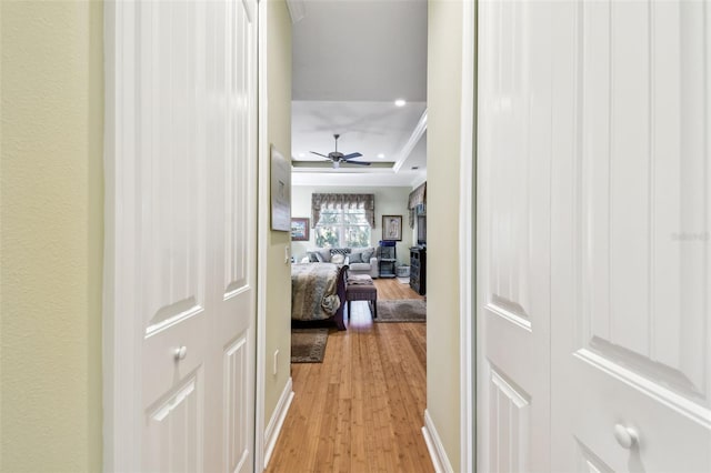 hall with ornamental molding, a tray ceiling, and light hardwood / wood-style flooring