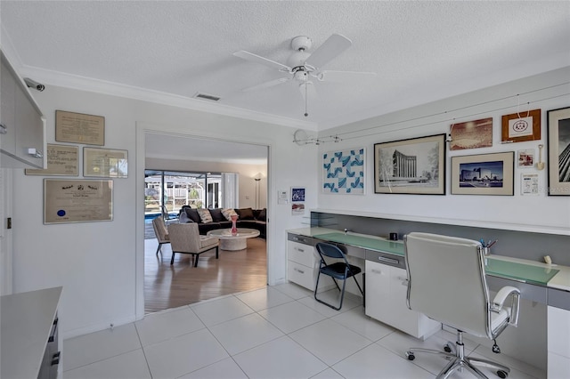 tiled home office with ceiling fan, crown molding, built in desk, and a textured ceiling