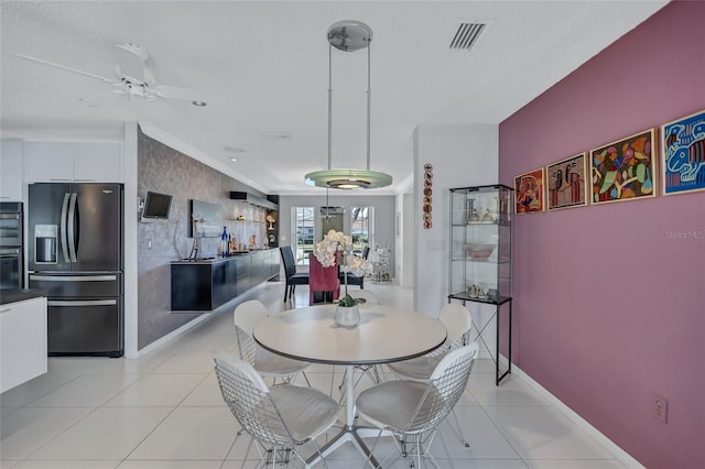 tiled dining space with ceiling fan and ornamental molding