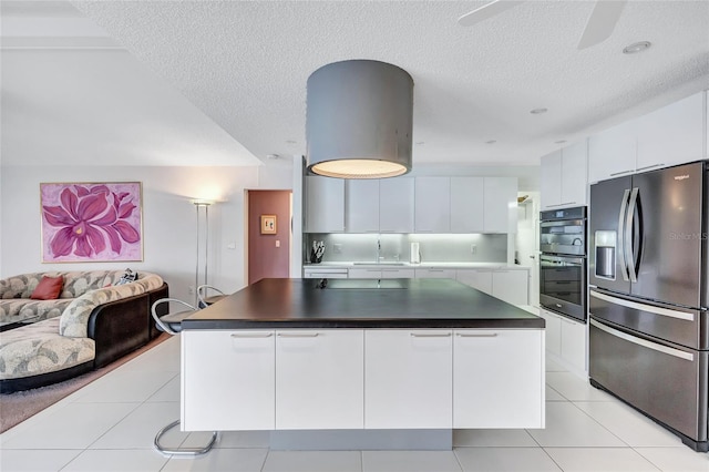 kitchen with light tile patterned flooring, sink, white cabinetry, a kitchen island, and stainless steel appliances