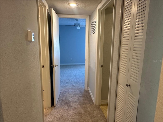 hallway with light colored carpet and a textured ceiling