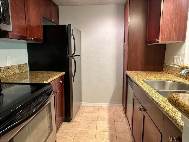 kitchen with appliances with stainless steel finishes, sink, light tile patterned floors, light stone counters, and a textured ceiling