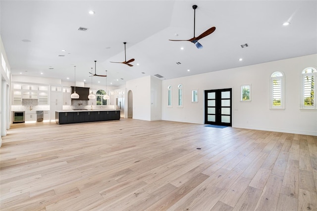 unfurnished living room featuring high vaulted ceiling, light hardwood / wood-style flooring, wine cooler, ceiling fan, and french doors