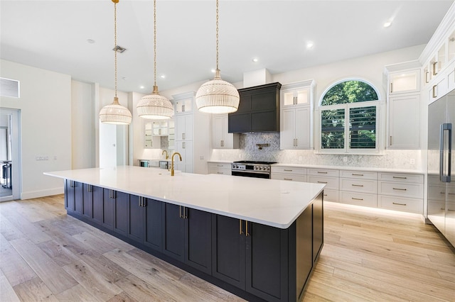 kitchen with decorative light fixtures, a large island with sink, white cabinets, and appliances with stainless steel finishes