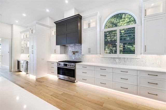 kitchen featuring high end stainless steel range oven, white cabinetry, tasteful backsplash, and light wood-type flooring