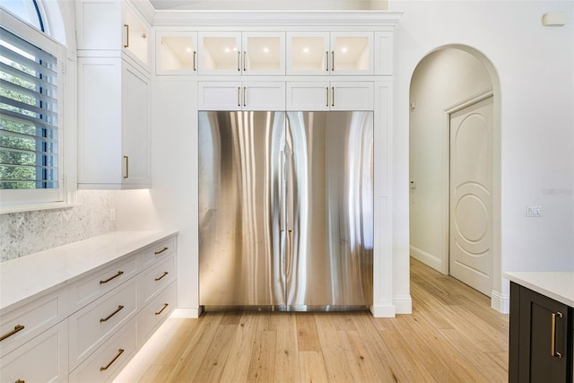 kitchen with white cabinets, stainless steel fridge, backsplash, and light hardwood / wood-style flooring