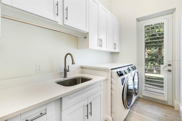 clothes washing area featuring light hardwood / wood-style floors, sink, cabinets, and washer and dryer