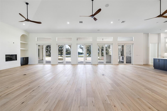 unfurnished living room with built in shelves, light hardwood / wood-style flooring, french doors, and ceiling fan