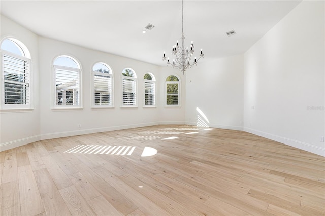 spare room featuring an inviting chandelier, light hardwood / wood-style flooring, and plenty of natural light