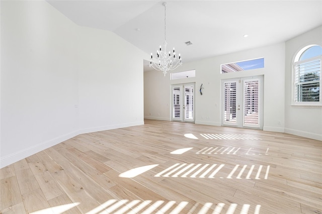 spare room featuring a notable chandelier, vaulted ceiling, french doors, and light wood-type flooring