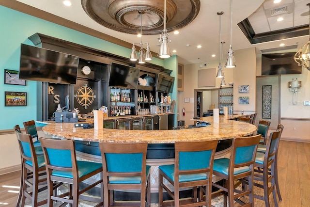 bar featuring crown molding, wood-type flooring, a raised ceiling, pendant lighting, and light stone countertops