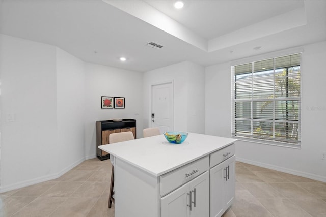 kitchen with a center island, light tile patterned floors, a tray ceiling, a kitchen breakfast bar, and white cabinets