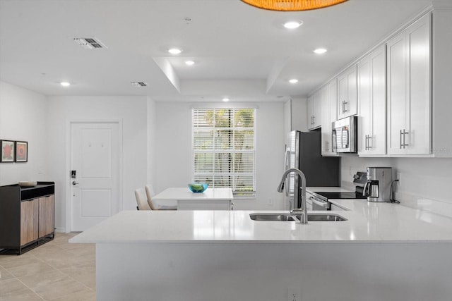 kitchen with sink, white cabinetry, stainless steel appliances, a raised ceiling, and kitchen peninsula