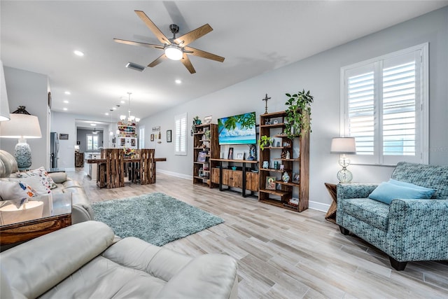 living room with plenty of natural light, ceiling fan with notable chandelier, and light wood-type flooring