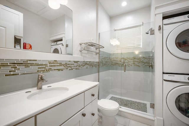 bathroom featuring walk in shower, toilet, vanity, stacked washing maching and dryer, and backsplash