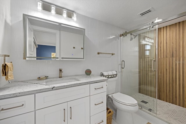 bathroom with vanity, toilet, a textured ceiling, and a shower with shower door