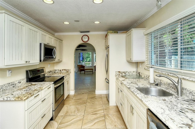 kitchen featuring sink, stainless steel appliances, ornamental molding, light stone countertops, and a textured ceiling