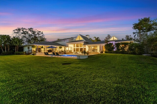 back house at dusk with a patio and a yard