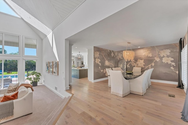 dining space featuring a skylight, high vaulted ceiling, a chandelier, and light hardwood / wood-style flooring