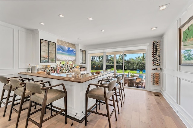 kitchen featuring butcher block counters, light wood-type flooring, a kitchen breakfast bar, kitchen peninsula, and white cabinets