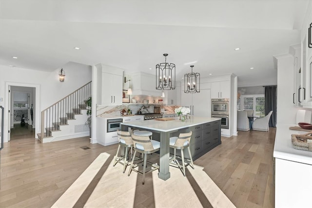 kitchen with a breakfast bar area, double oven, a center island, white cabinets, and decorative light fixtures