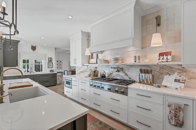 kitchen featuring white cabinetry, sink, backsplash, hanging light fixtures, and stainless steel gas cooktop