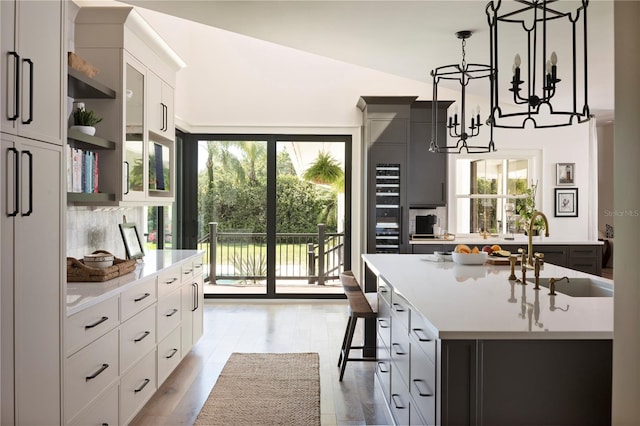 kitchen featuring sink, white cabinetry, an island with sink, pendant lighting, and hardwood / wood-style floors