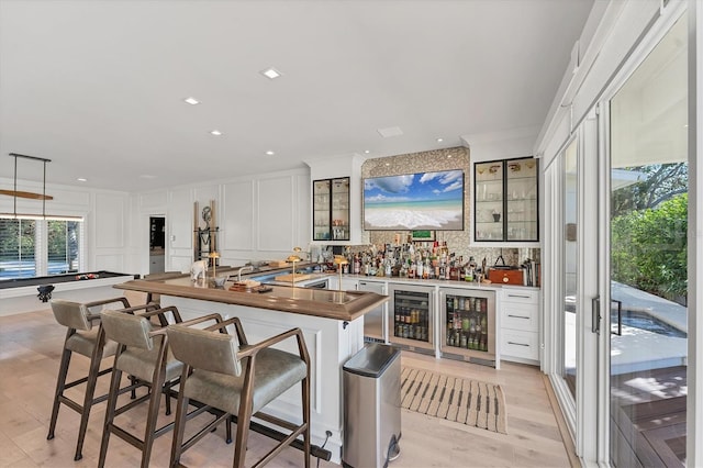 bar featuring pendant lighting, white cabinets, wine cooler, ornamental molding, and light wood-type flooring