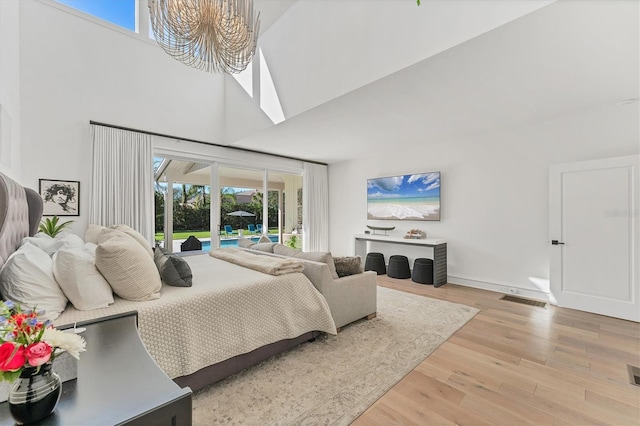 bedroom featuring hardwood / wood-style flooring, a towering ceiling, access to exterior, and a chandelier