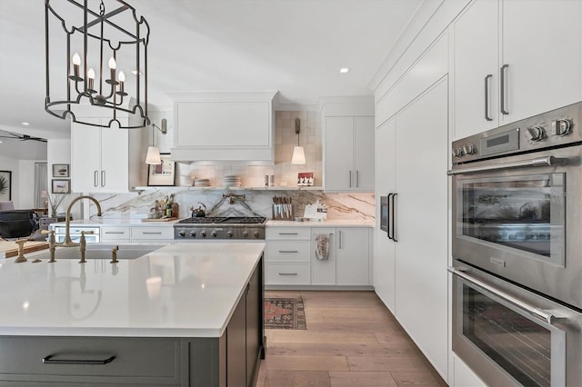 kitchen with sink, custom exhaust hood, white cabinetry, an island with sink, and stainless steel appliances