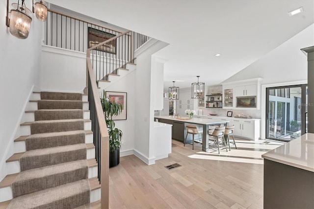 staircase featuring high vaulted ceiling, hardwood / wood-style floors, and a notable chandelier