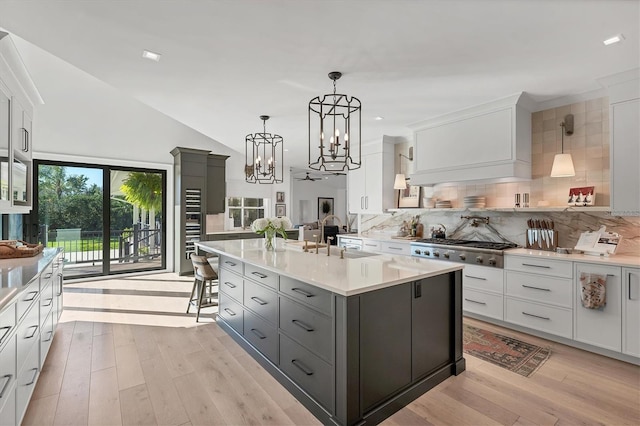 kitchen with stainless steel gas cooktop, white cabinetry, hanging light fixtures, a center island with sink, and gray cabinets