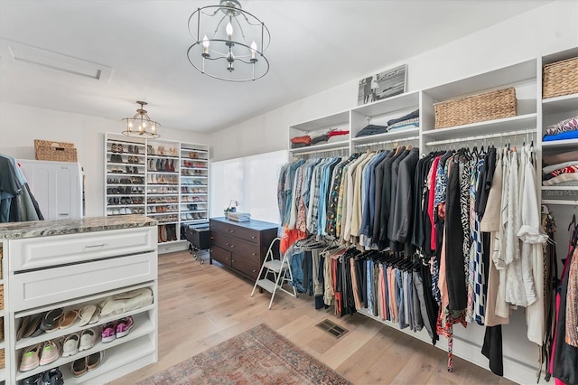 walk in closet with a chandelier and light hardwood / wood-style floors