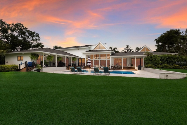 back of property at dusk with a patio, a yard, and an outdoor pool