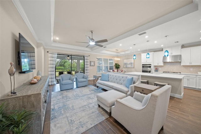 living room featuring crown molding, a tray ceiling, and ceiling fan with notable chandelier