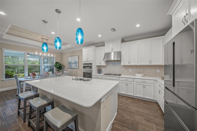 kitchen featuring appliances with stainless steel finishes, decorative light fixtures, an island with sink, and white cabinets