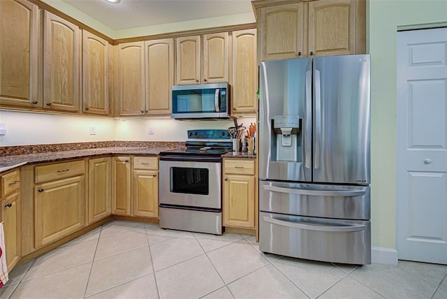 kitchen featuring dark stone countertops, appliances with stainless steel finishes, light tile patterned floors, and light brown cabinetry