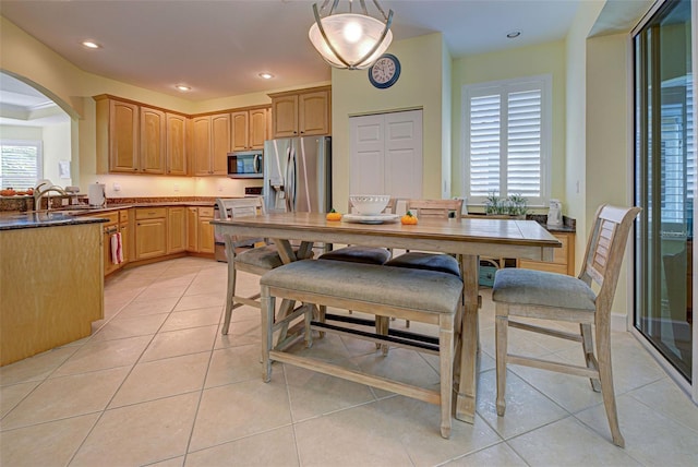 kitchen featuring stainless steel appliances, light tile patterned floors, light brown cabinetry, and decorative light fixtures