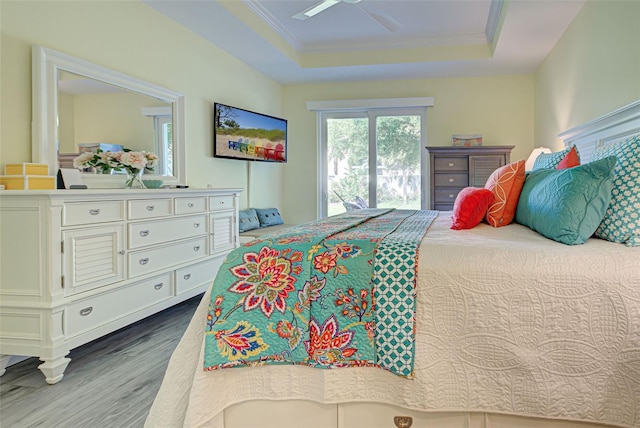 bedroom with crown molding, a tray ceiling, wood-type flooring, and ceiling fan