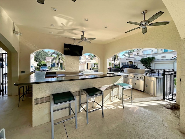 view of patio featuring a bar, ceiling fan, an outdoor kitchen, and grilling area