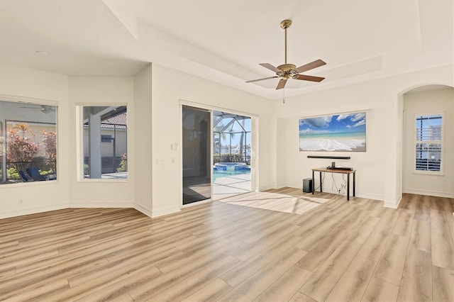 unfurnished living room featuring a raised ceiling, ceiling fan, and light wood-type flooring