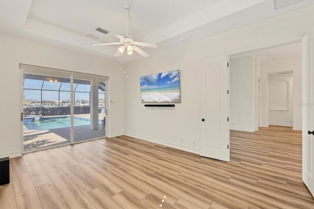 unfurnished living room featuring ceiling fan, light wood-type flooring, and a tray ceiling