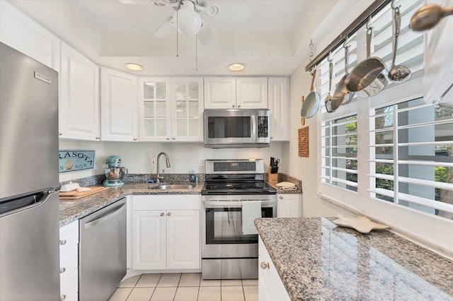 kitchen with sink, light tile patterned floors, appliances with stainless steel finishes, white cabinetry, and light stone counters