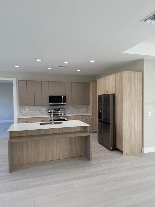 kitchen featuring appliances with stainless steel finishes, a kitchen island with sink, sink, and decorative backsplash